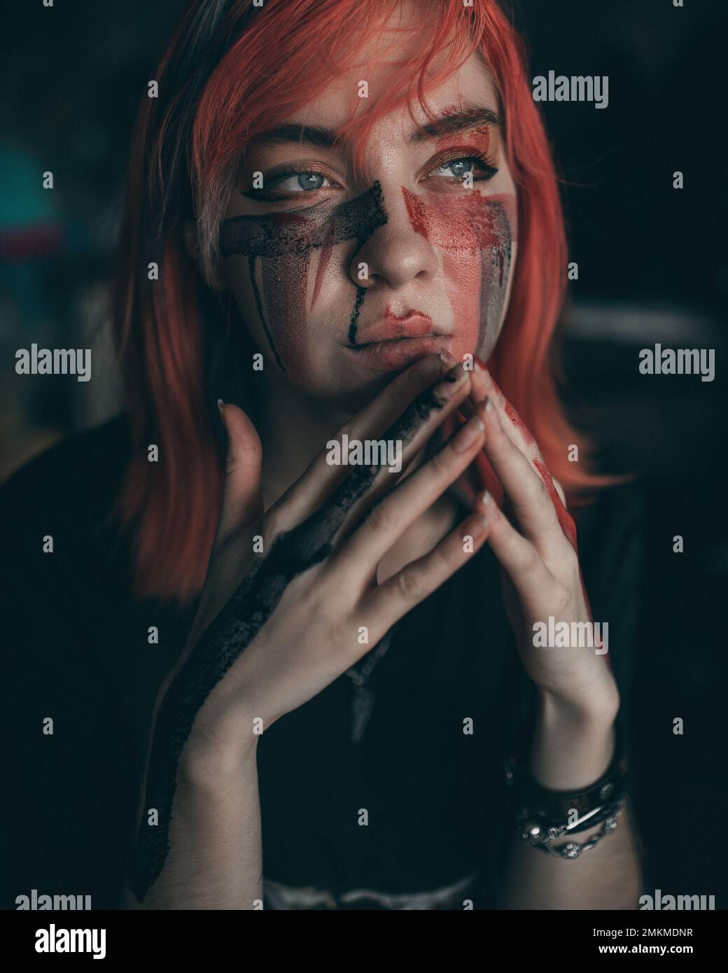 Young redhead woman artist applies red and black paint to her face with brush Stock Photo