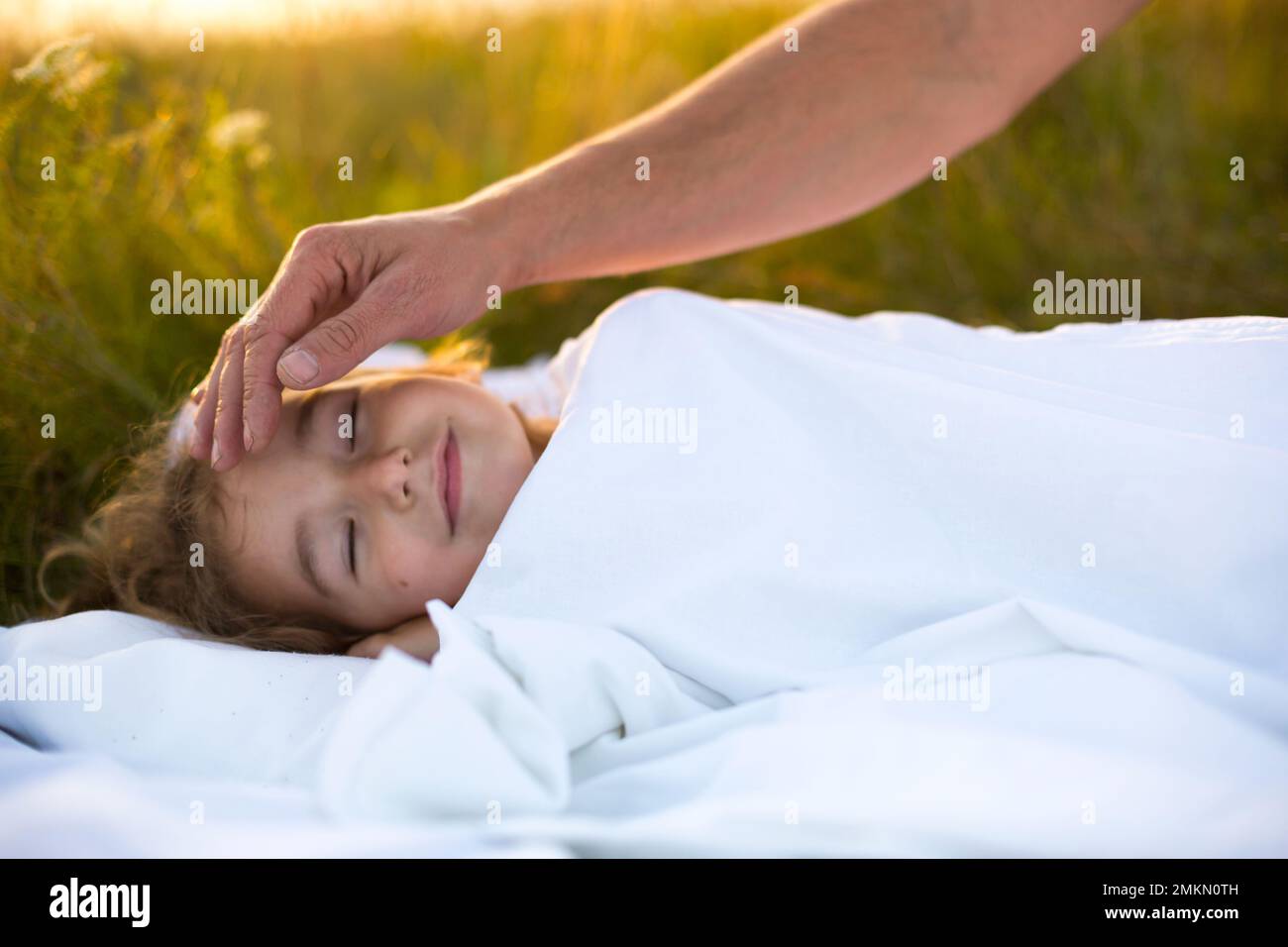Girl sleeps on white bed in the grass, fresh air. Dad's hand gently pats his head. Care, protection, International Children's Day, mosquito bites Stock Photo