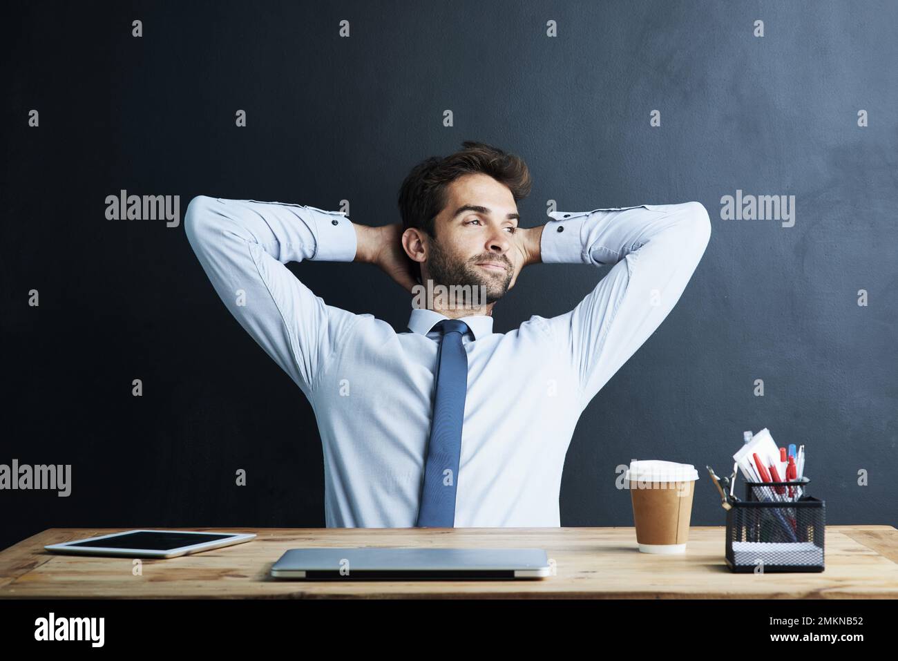 Dreaming about success. a young corporate businessman sitting at a desk against a dark background. Stock Photo