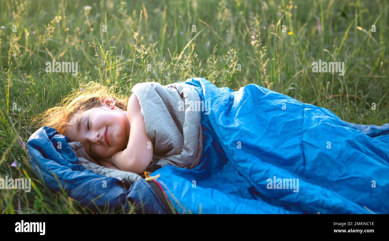 A child sleeps in a sleeping bag on the grass in a camping trip - eco-friendly outdoor recreation, healthy lifestyle, summer time. Sweet and peaceful Stock Photo