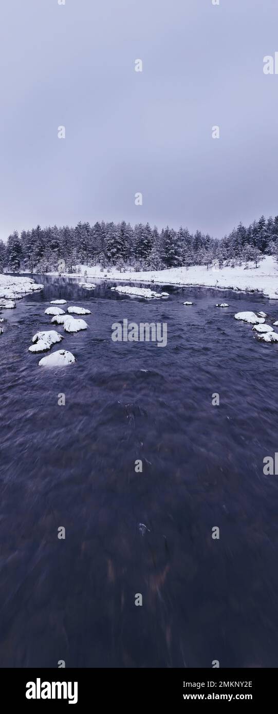 An aerial view of a frozen river flowing through snow-covered forests ...