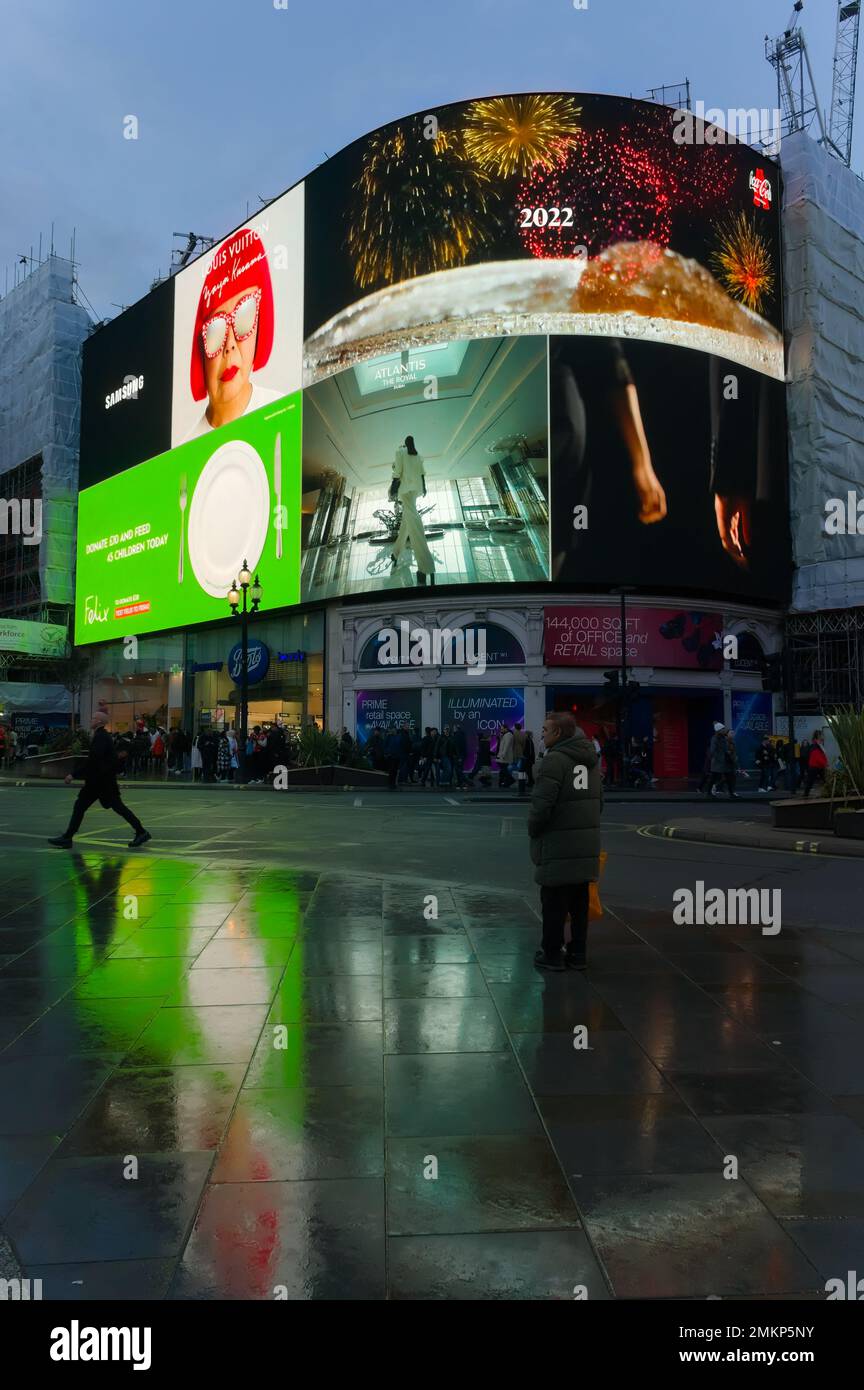 a man standing on the wet pavement with the famous advertising signs overhead in Piccadilly. Stock Photo