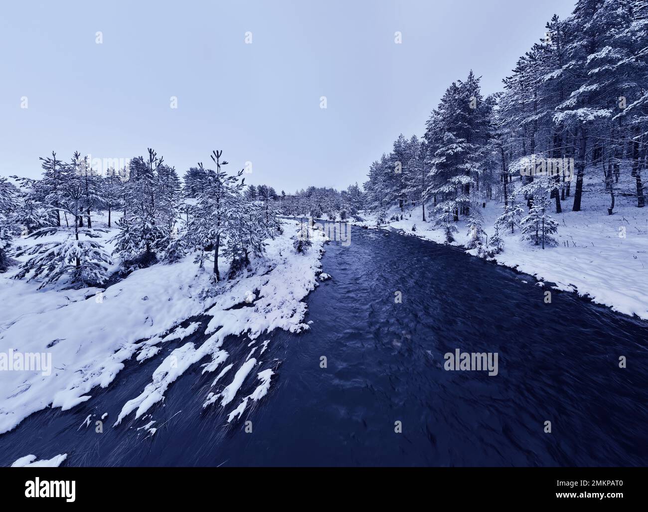 An aerial view of a frozen river flowing through snow-covered forests ...