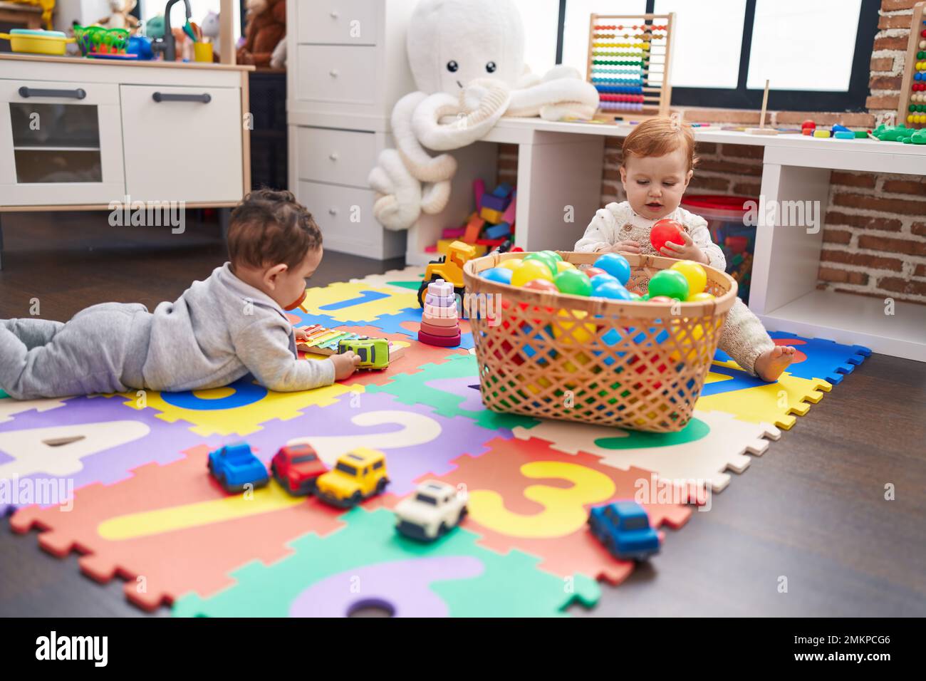 Two adorable babies playing with balls sitting on floor at kindergarten ...