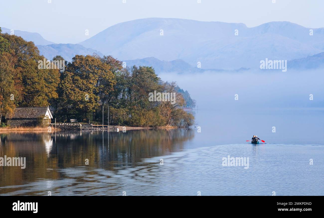LAKE DISTRICT, UK - October 12, 2010. Boat house on shore of Coniston Water with couple paddling a double canoe. Misty morning in autumn. Stock Photo