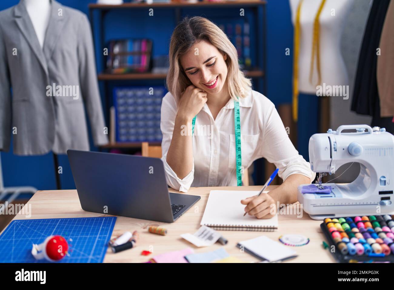 Young woman tailor drawing clothes on notebook at clothing factory ...