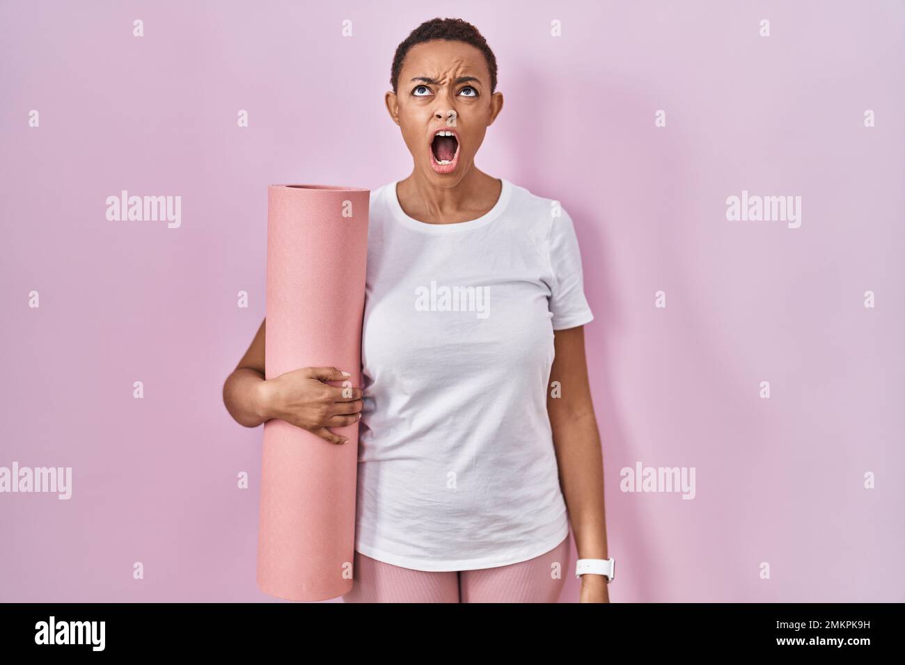 Beautiful african american woman holding yoga mat angry and mad ...