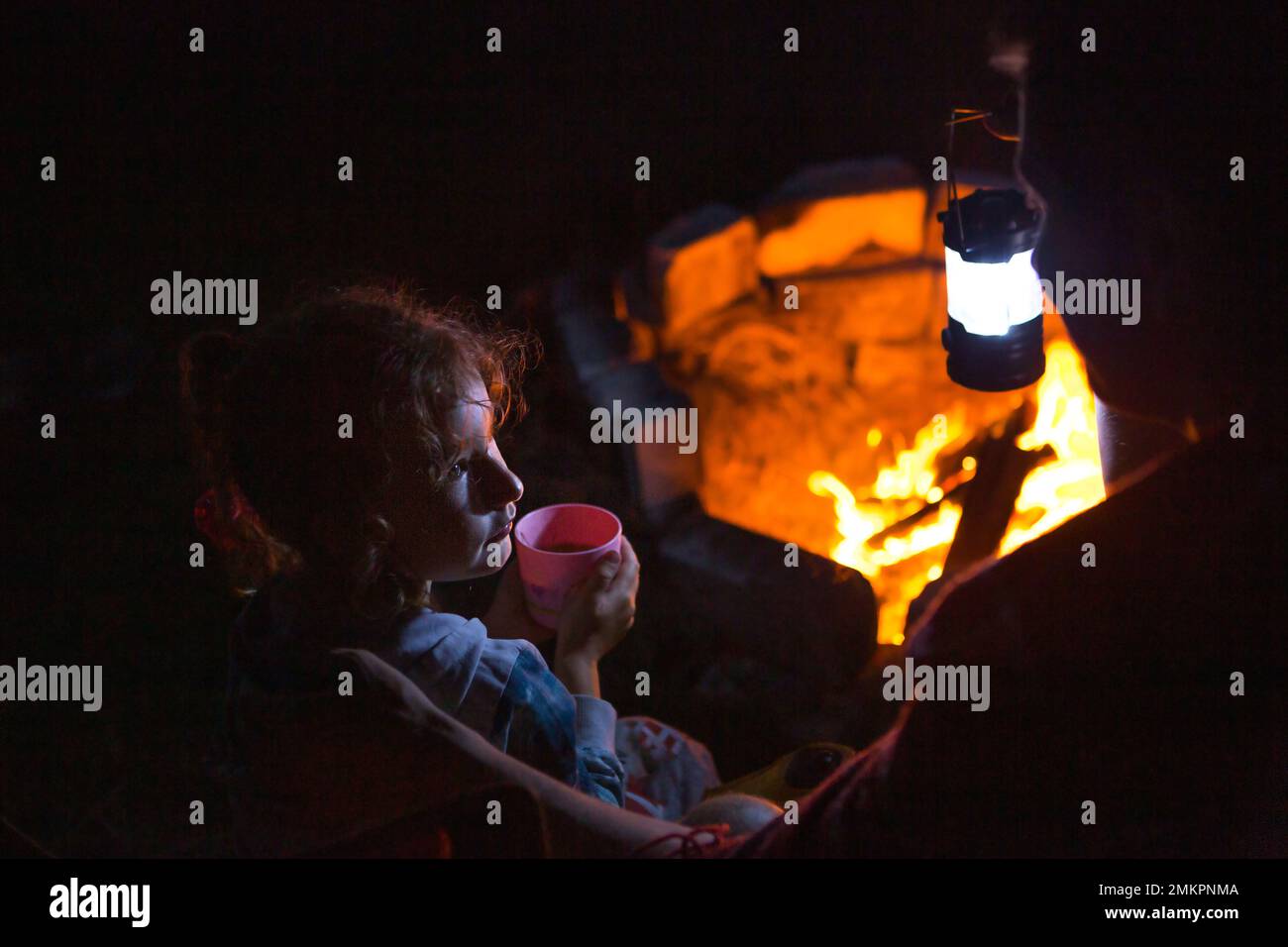 Dad and daughter sit at night by the fire in the open air in the summer ...