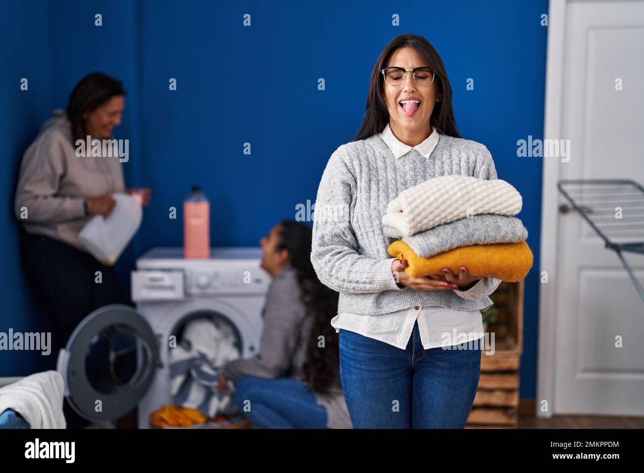Three women doing laundry at home sticking tongue out happy with funny expression. Stock Photo
