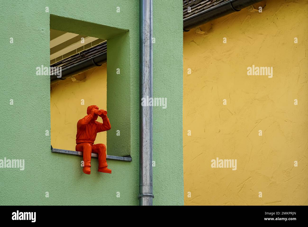 Residents have decorated a window bay of their loggia with a seated sculpture holding binoculars in front of its eyes in both hands spying Neighbors. Stock Photo