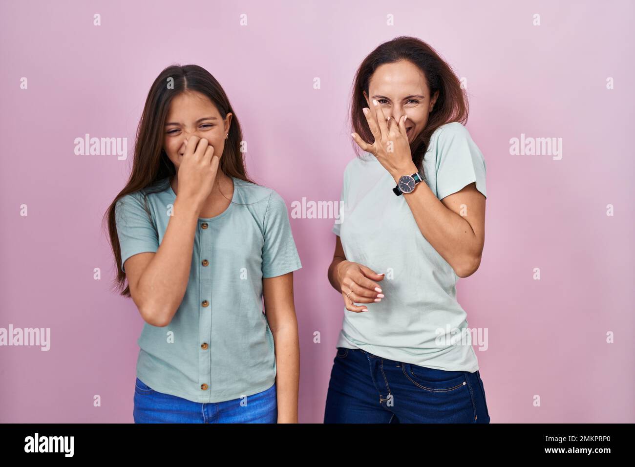 Young mother and daughter standing over pink background smelling