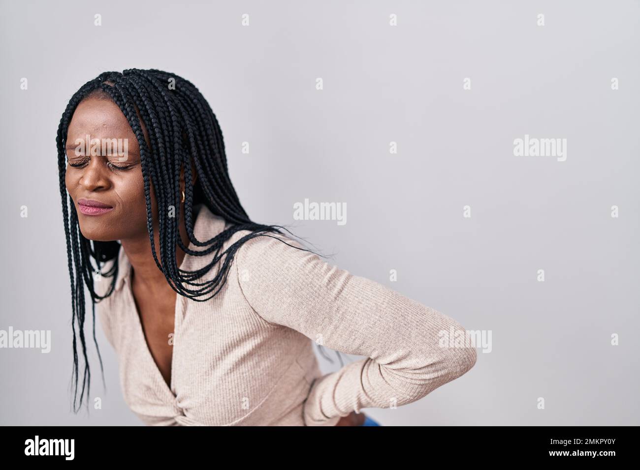 African woman with braids standing over white background suffering of backache, touching back