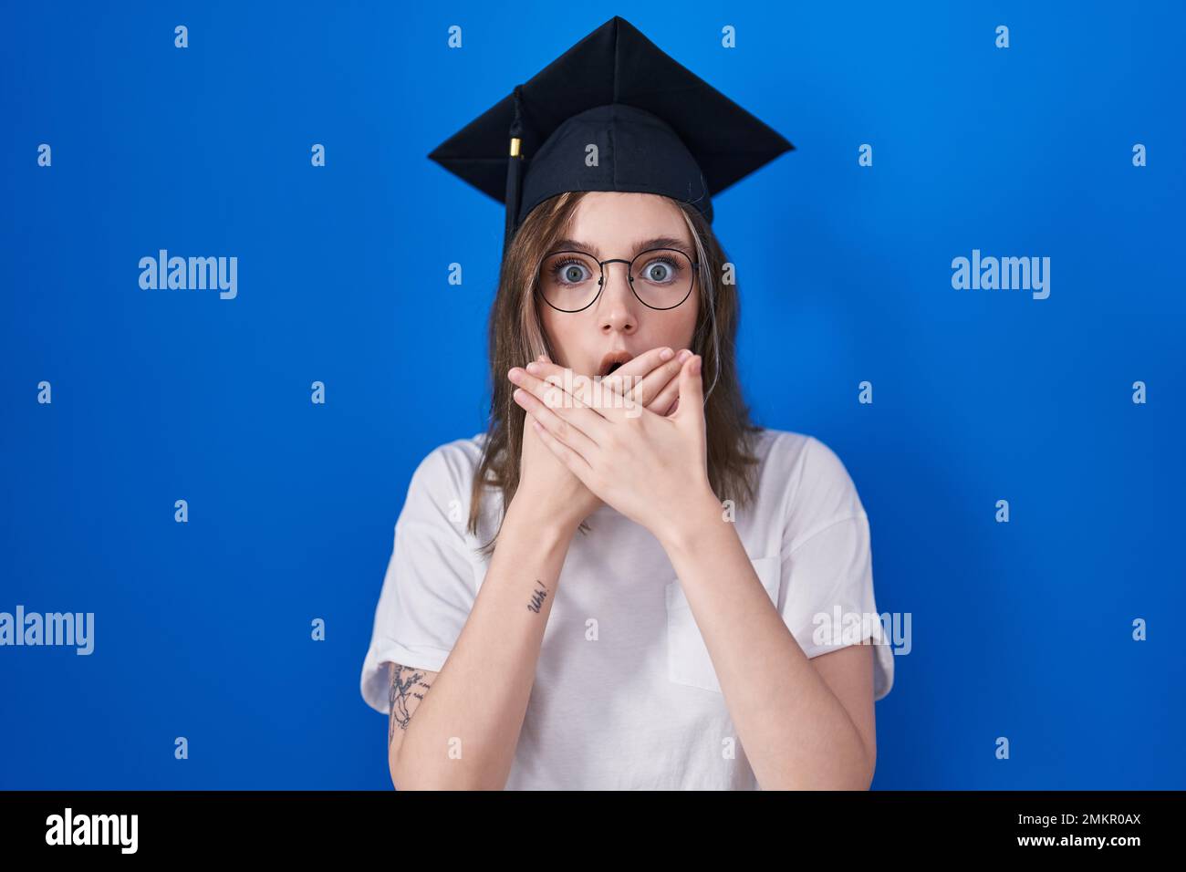 Blonde caucasian woman wearing graduation cap shocked covering mouth ...