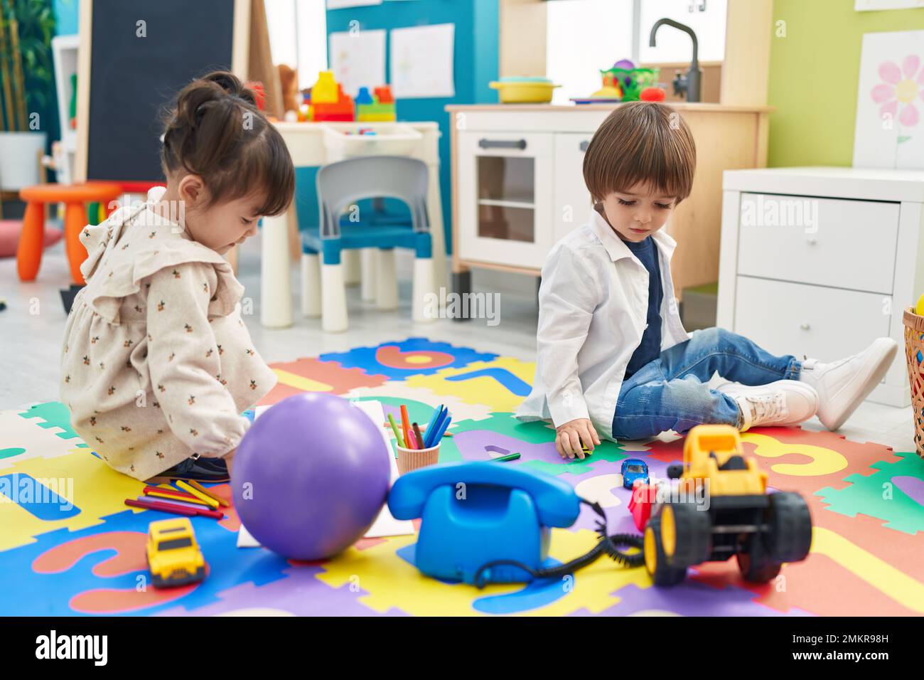 Two kids playing with toys sitting on floor at kindergarten Stock Photo ...