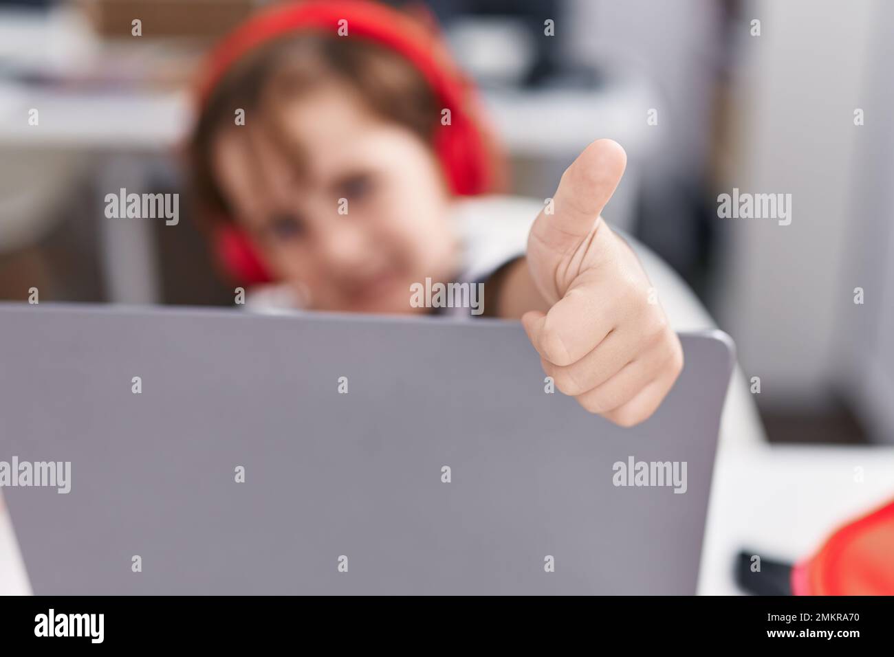 Adorable hispanic boy student using laptop doing ok gesture with thumb ...