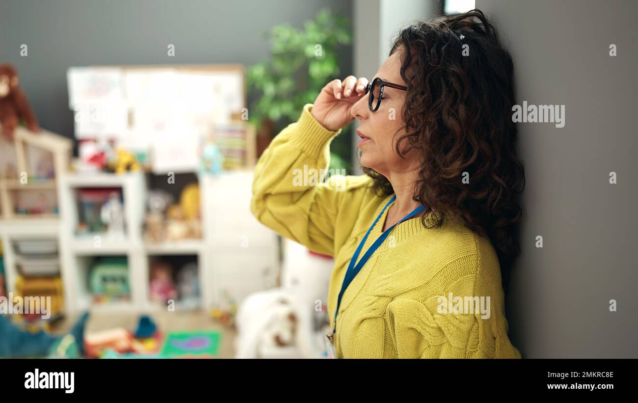 Middle age hispanic woman preschool teacher stressed standing at kindergarten Stock Photo