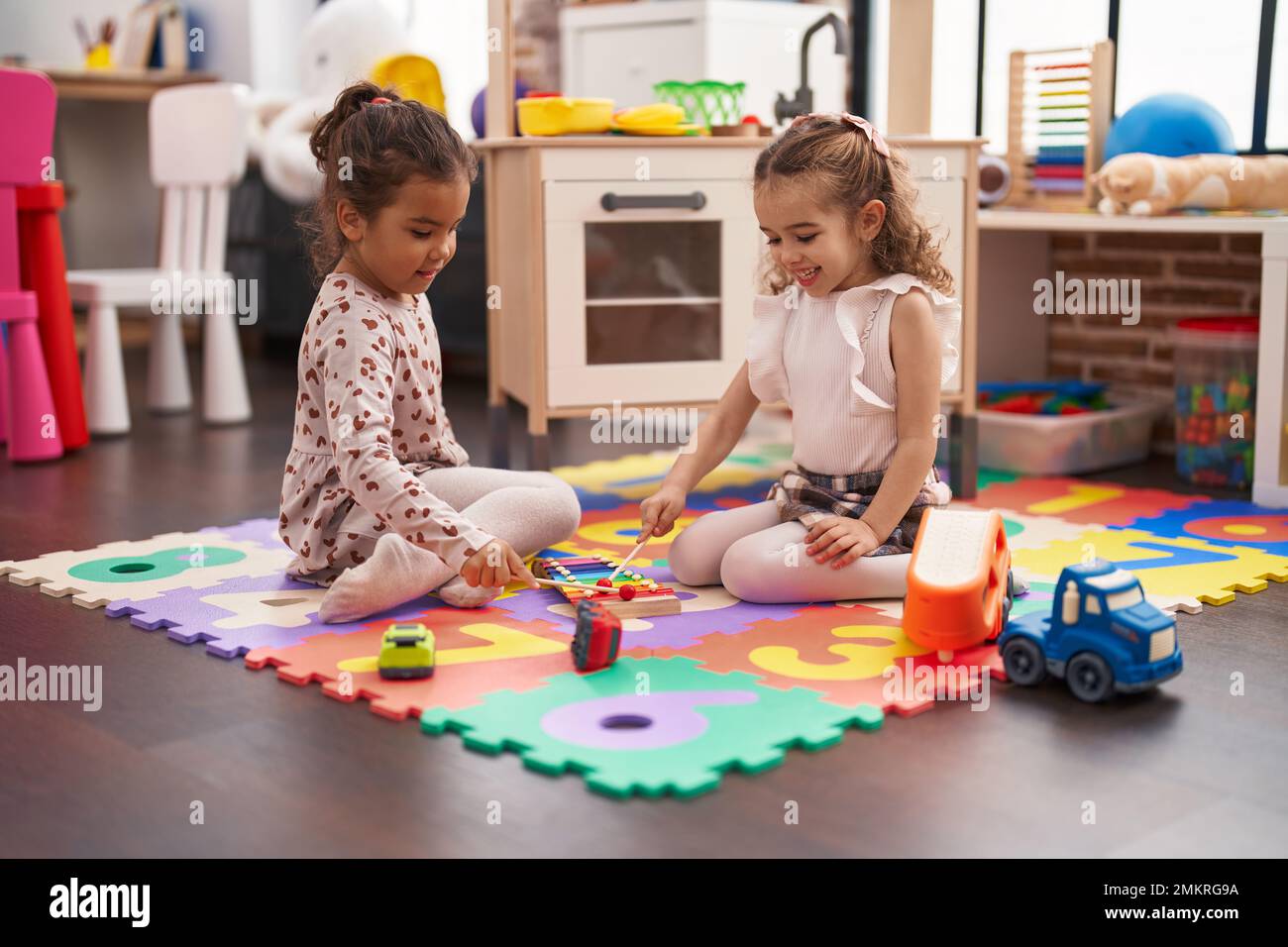 Two kids playing xylophone sitting on floor at kindergarten Stock Photo