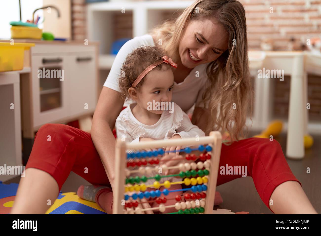 Teacher and toddler learning maths with abacus sitting on floor at