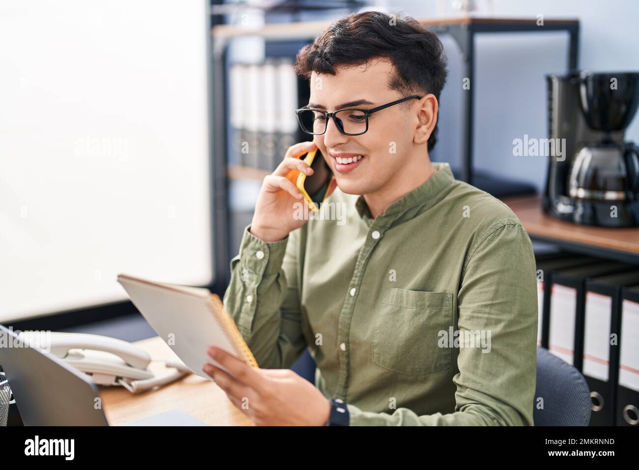 Young non binary man business worker talking on telephone reading ...