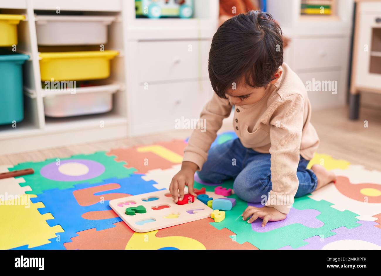 Adorable hispanic boy playing with maths puzzle game sitting on floor ...