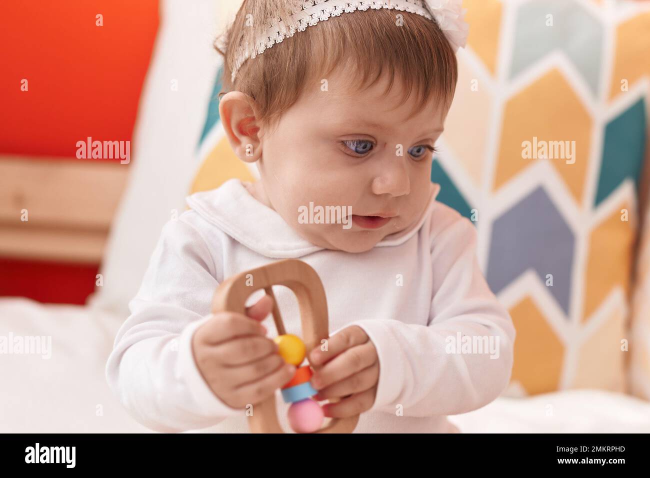 Adorable blonde baby holding toy sitting on bed at bedroom Stock Photo ...