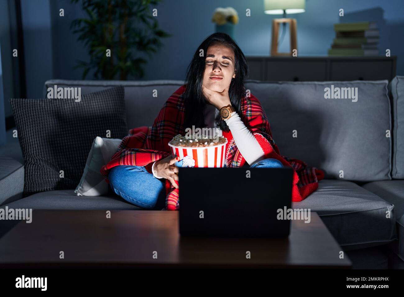 Hispanic woman eating popcorn watching a movie on the sofa touching
