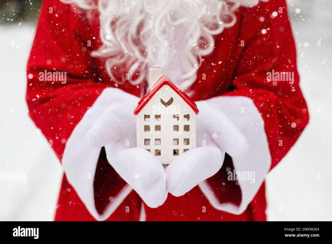 House, miniature cottage in hands of Santa Claus outdoor in snow. Deal for real estate, purchase, construction, relocation, mortgage. Cozy home, Deliv Stock Photo