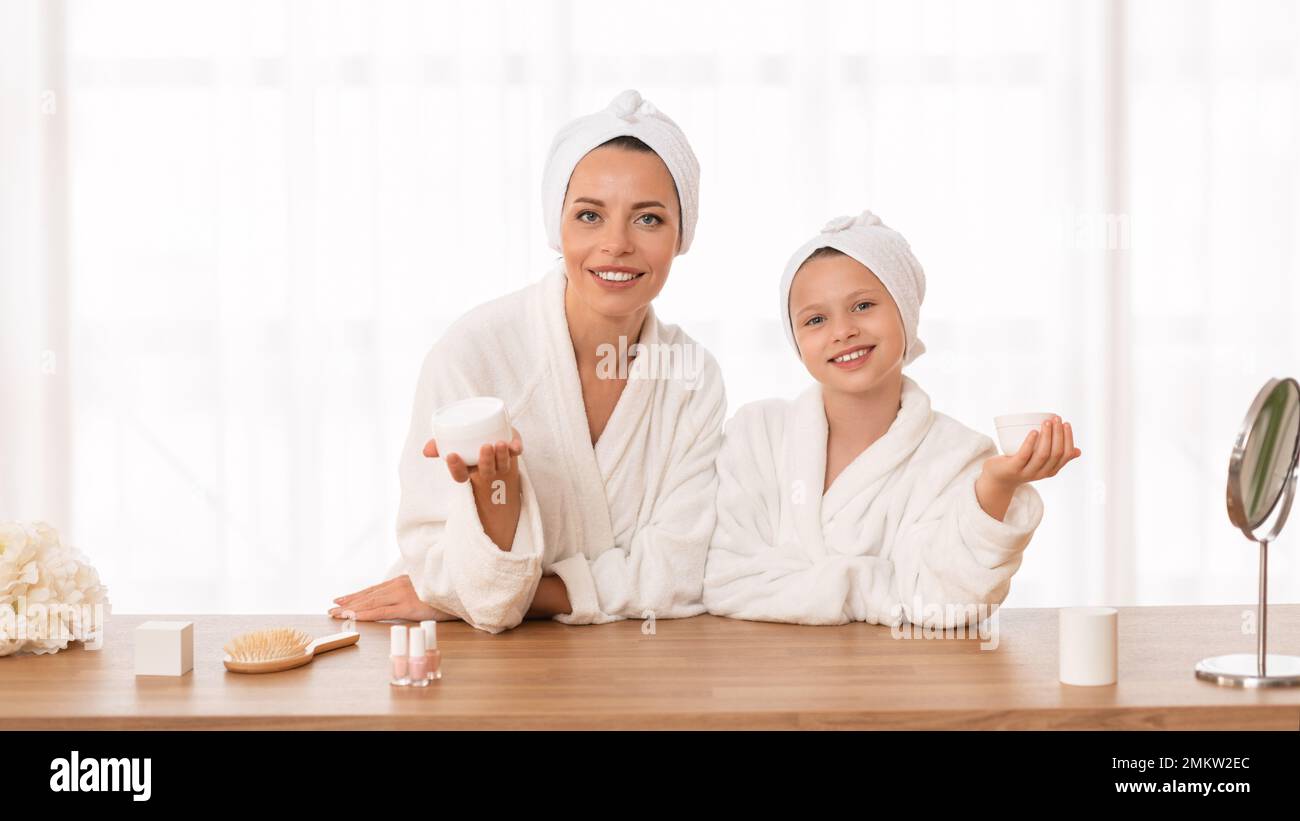 Skin Care Concept. Mother And Little Daughter Wearing Bathrobes Holding Moisturising Cream Stock Photo
