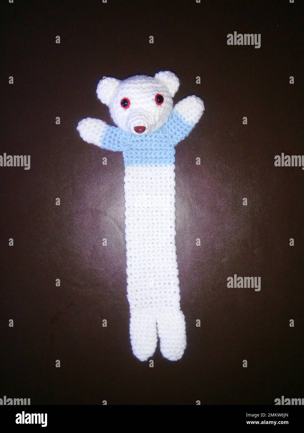 Crocheted teddy bear bookmark wearing a pale blue jumper. Hand made bookmark, arts and crafts. Stock Photo