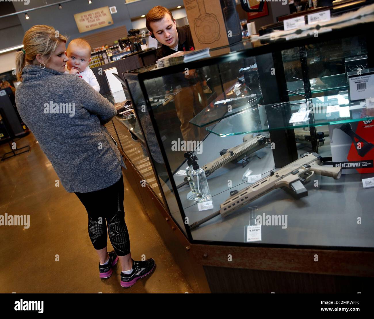 In this photo taken Friday, Dec. 21, 2108, a salesperson points out  features on a handgun for Anne Vifquain while she holds her son Gavin, 1,  at Frontier Justice in Lee's Summit,