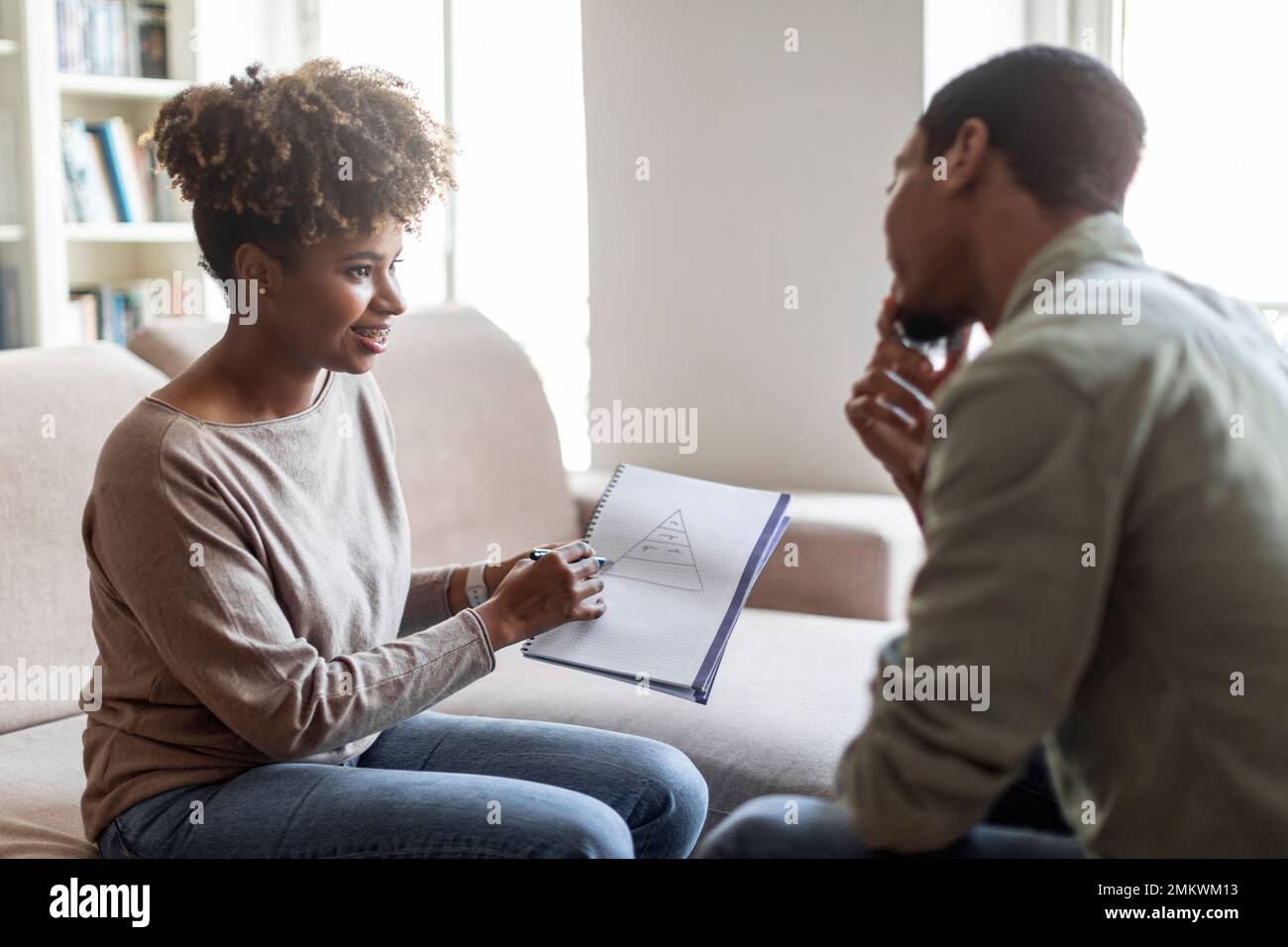 Young black woman psychologist having conversation with patient, showing notes Stock Photo