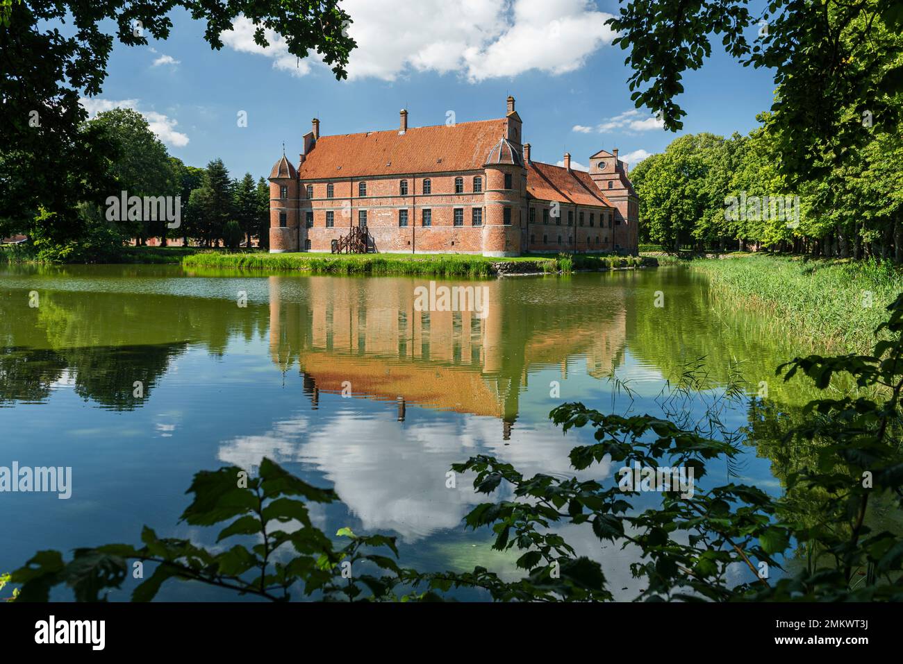 Denmark, Jutland, Djursland: The Renaissance facade of Rosenholm Castle reflected in the water and framed by leaves and branches Stock Photo