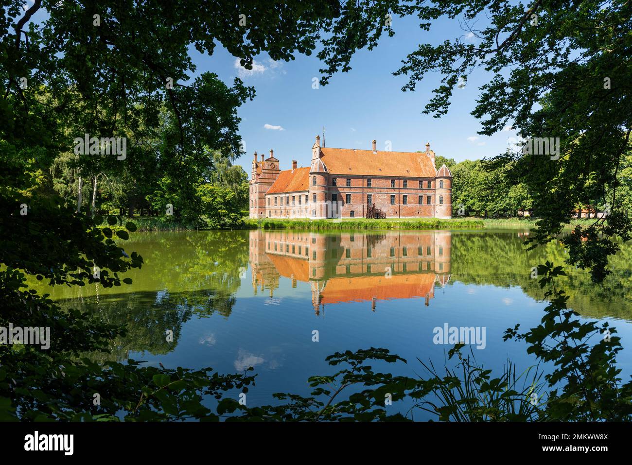 Denmark, Jutland, Djursland: The Renaissance facade of Rosenholm Castle reflected in the water and framed by leaves and branches Stock Photo