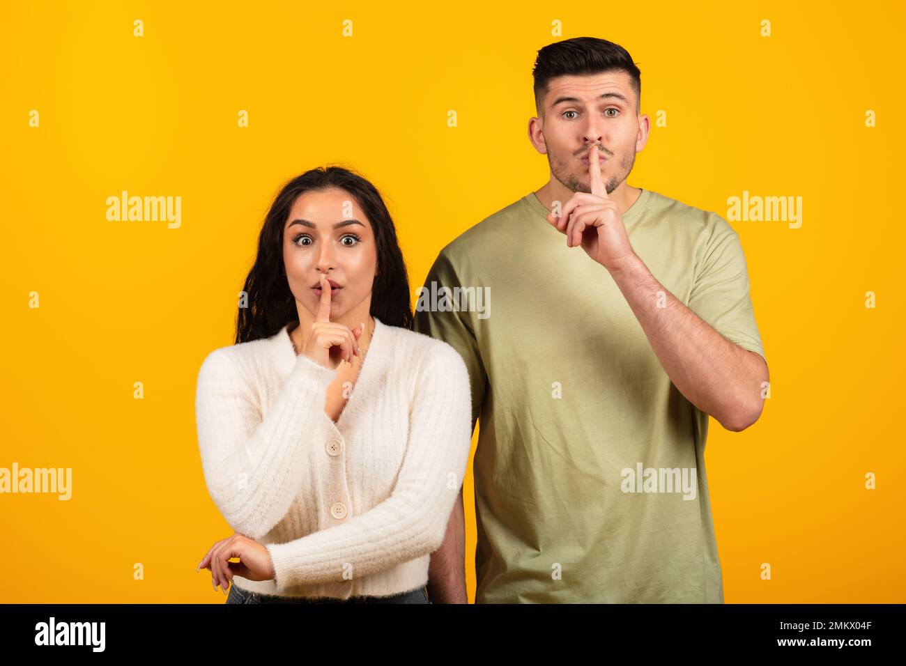 Cheerful inspired pretty young arabic woman and guy in casual put finger to lips, make shhh sign Stock Photo