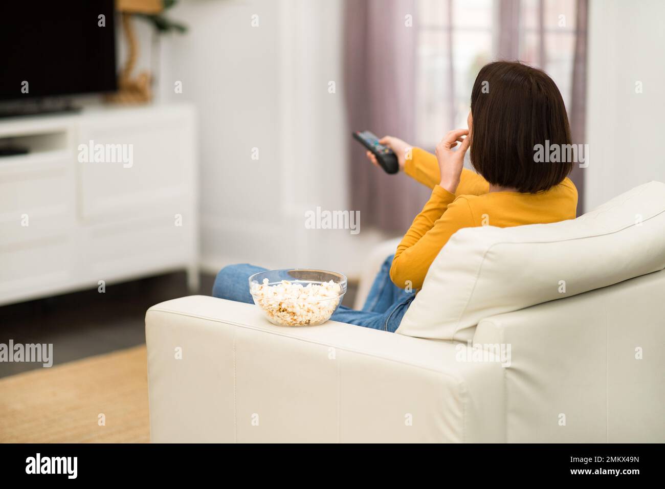 Rear view of woman watching TV with popcorn at home Stock Photo