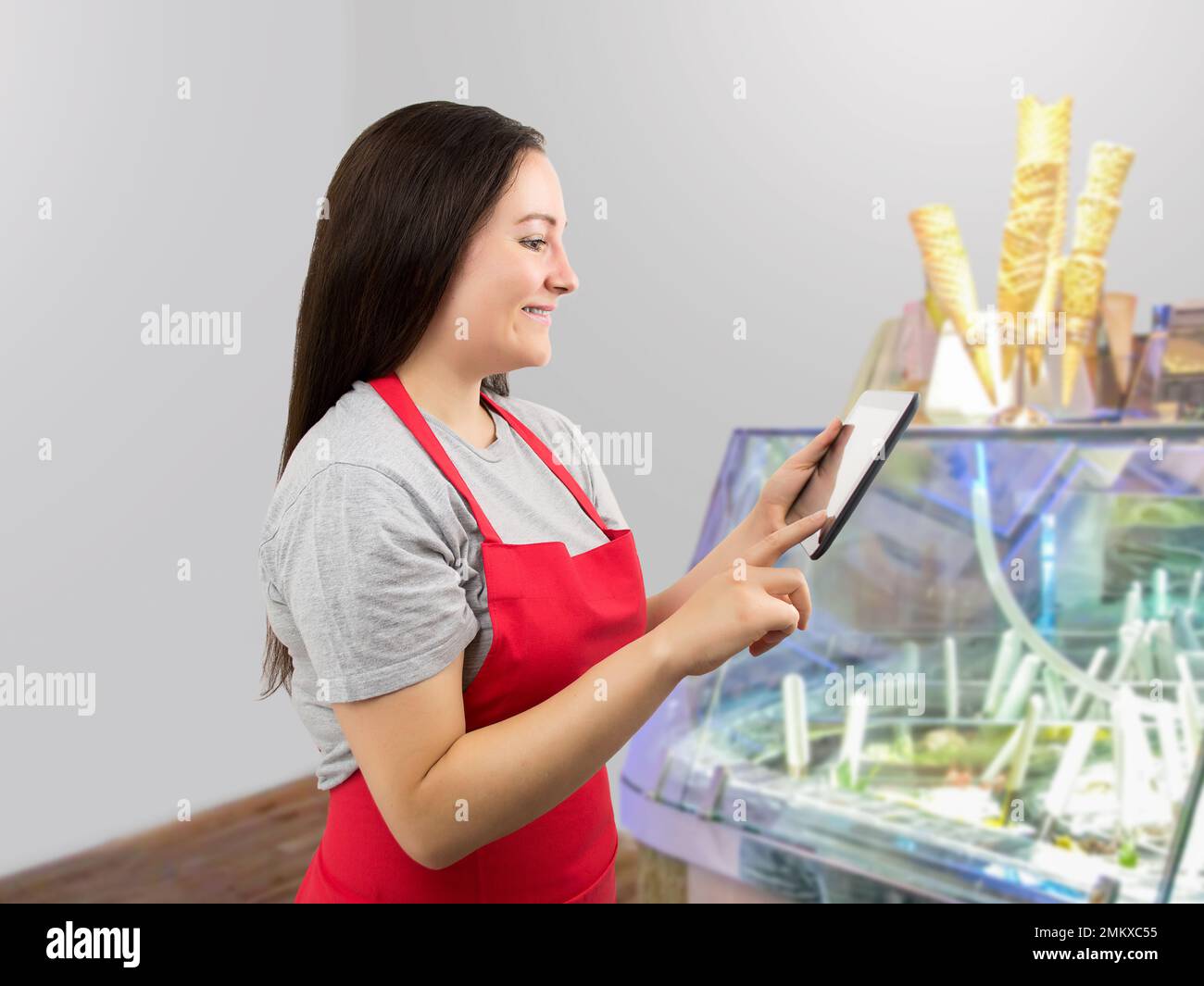 Smiling ice cream store employee standing behind the counter in the store and uses a digital tablet Stock Photo