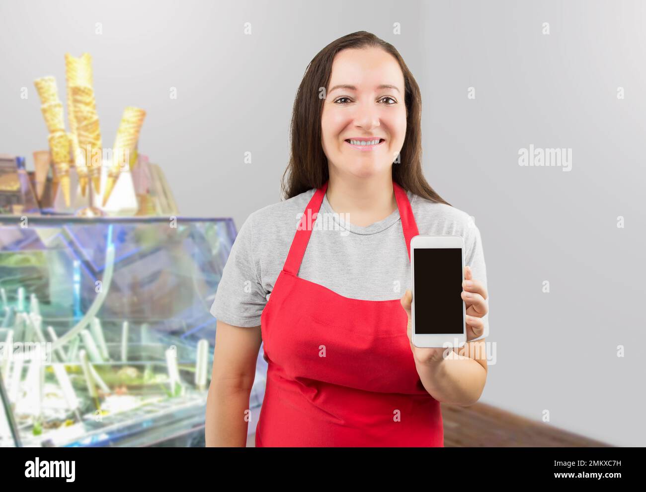 Smiling ice cream store employee standing behind the counter in the store and showing a phone Stock Photo
