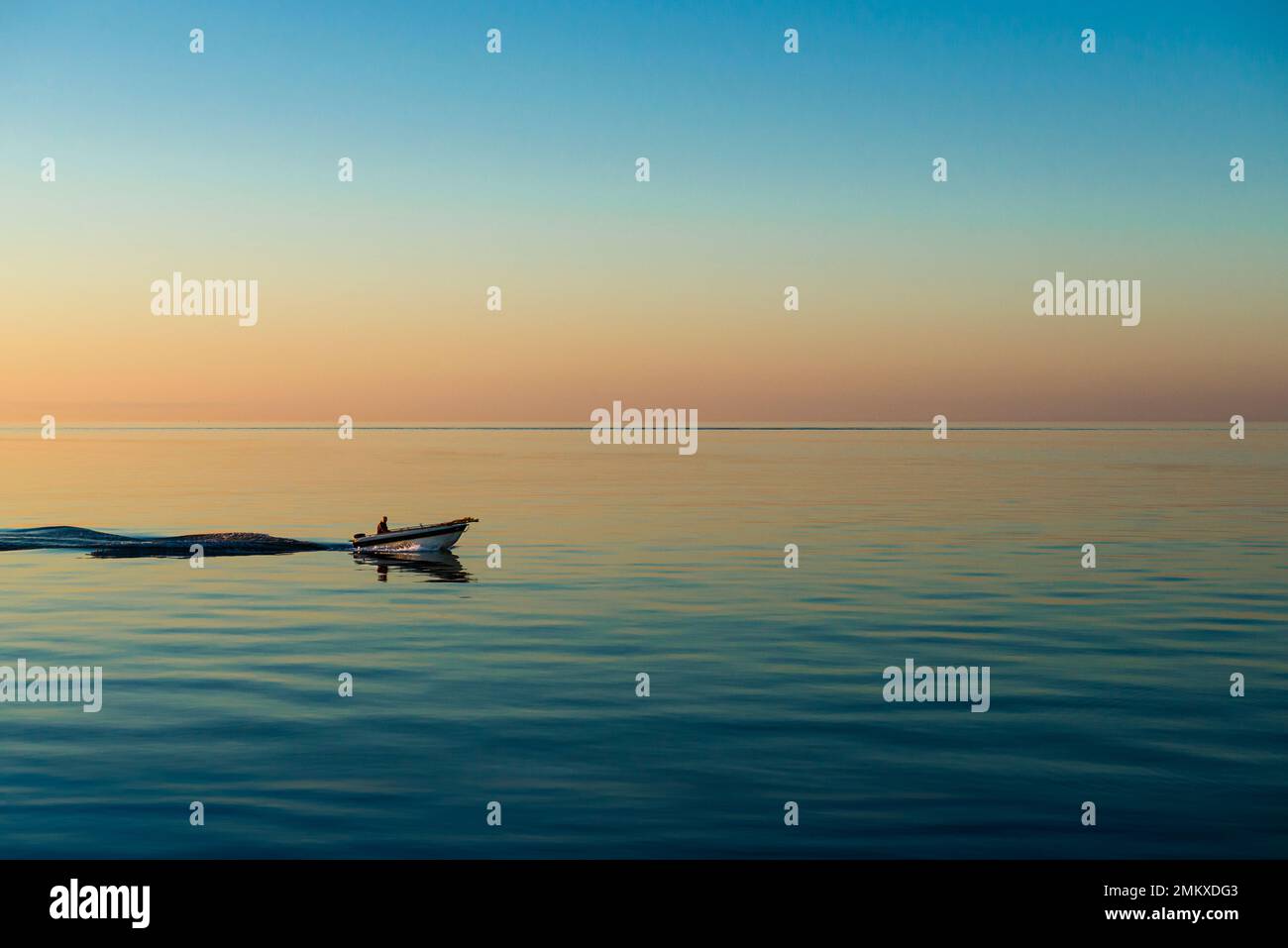 A fisherman drives his motor boat through the calm sea on the coast of Jutland against the colourful sky of a summer dawn, Djursland, Denmark Stock Photo