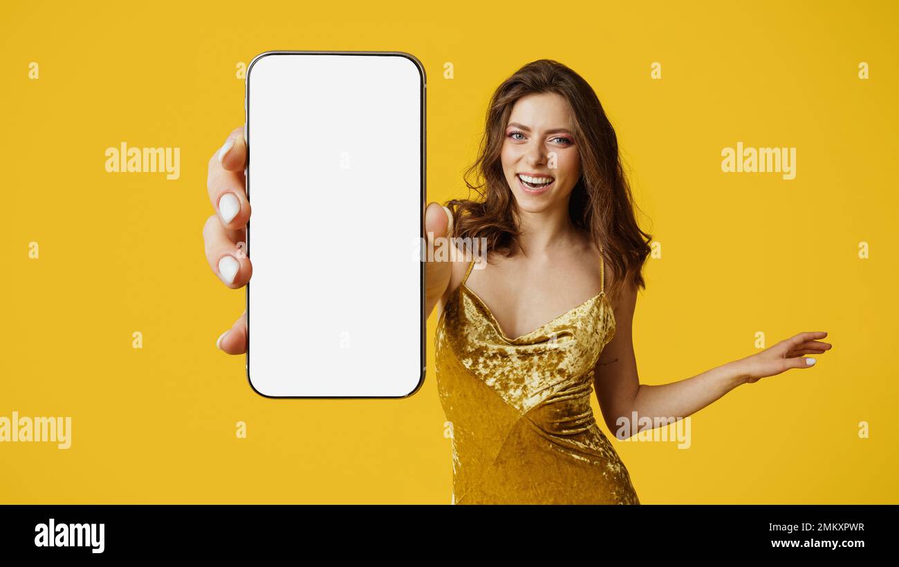 Cheery woman showing modern smartphone with empty screen, advertising new app or website, wearing dress, mockup Stock Photo