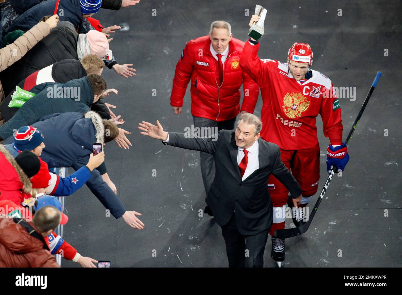 Russian Ice Hockey Federation president Vladislav Tretyak, front, followed by Russias Evgeny Ketov holding the Channel One Cup trophy, as they leave the rink after the Channel One Cup ice hockey match