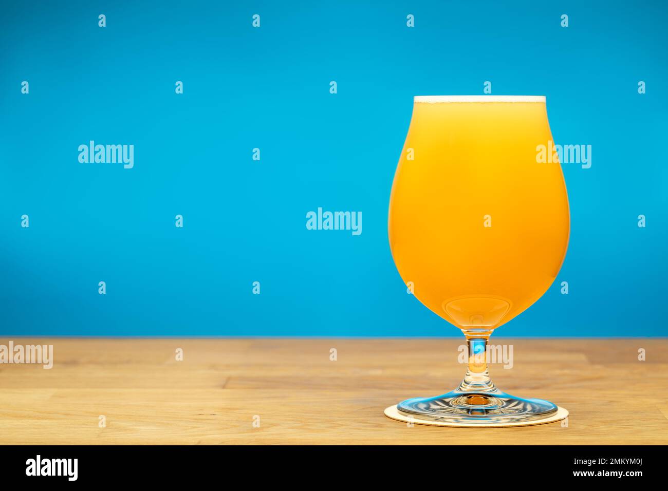 Full snifter glass of hazy New England IPA (NEIPA) pale ale beer on wooden table with blue background Stock Photo