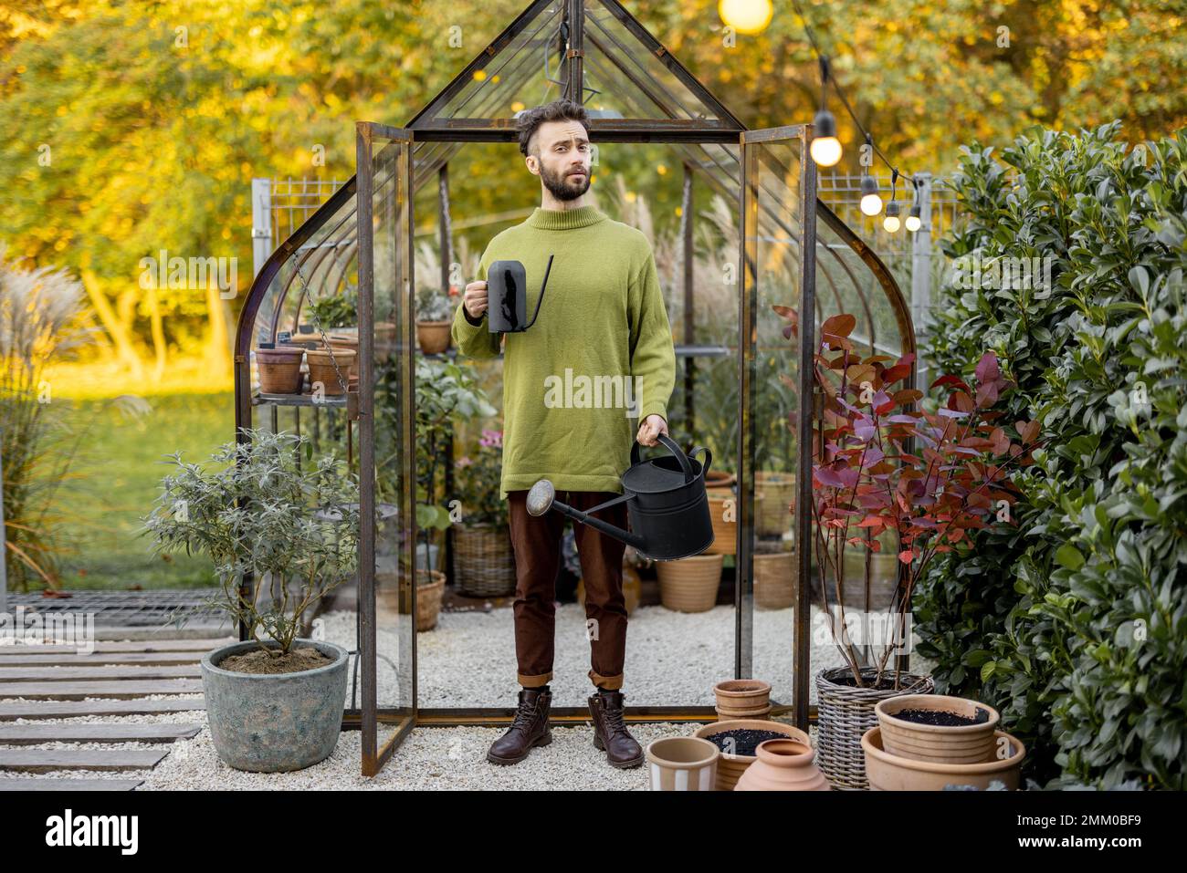 Stylish guy with watering can in garden Stock Photo