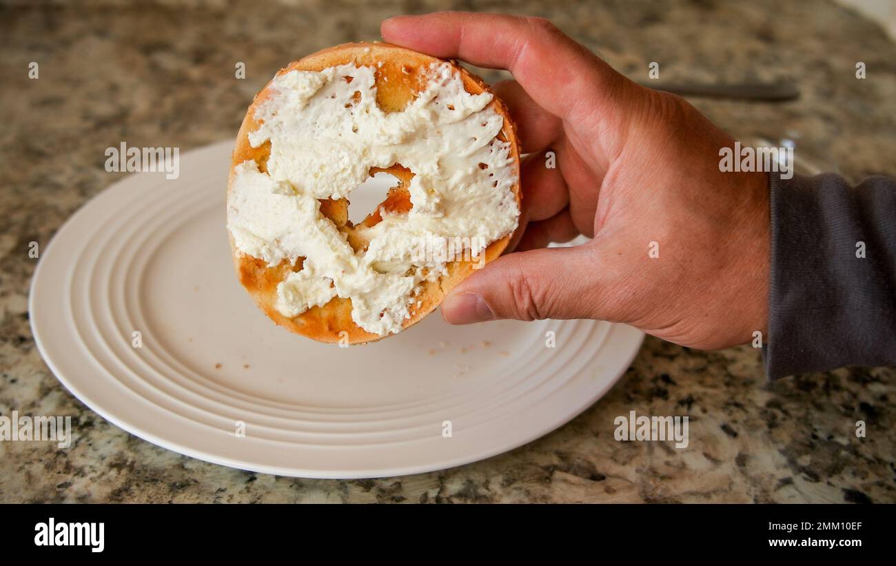 Hand holding toasted bagel with butter and whipped cheese cream Stock Photo