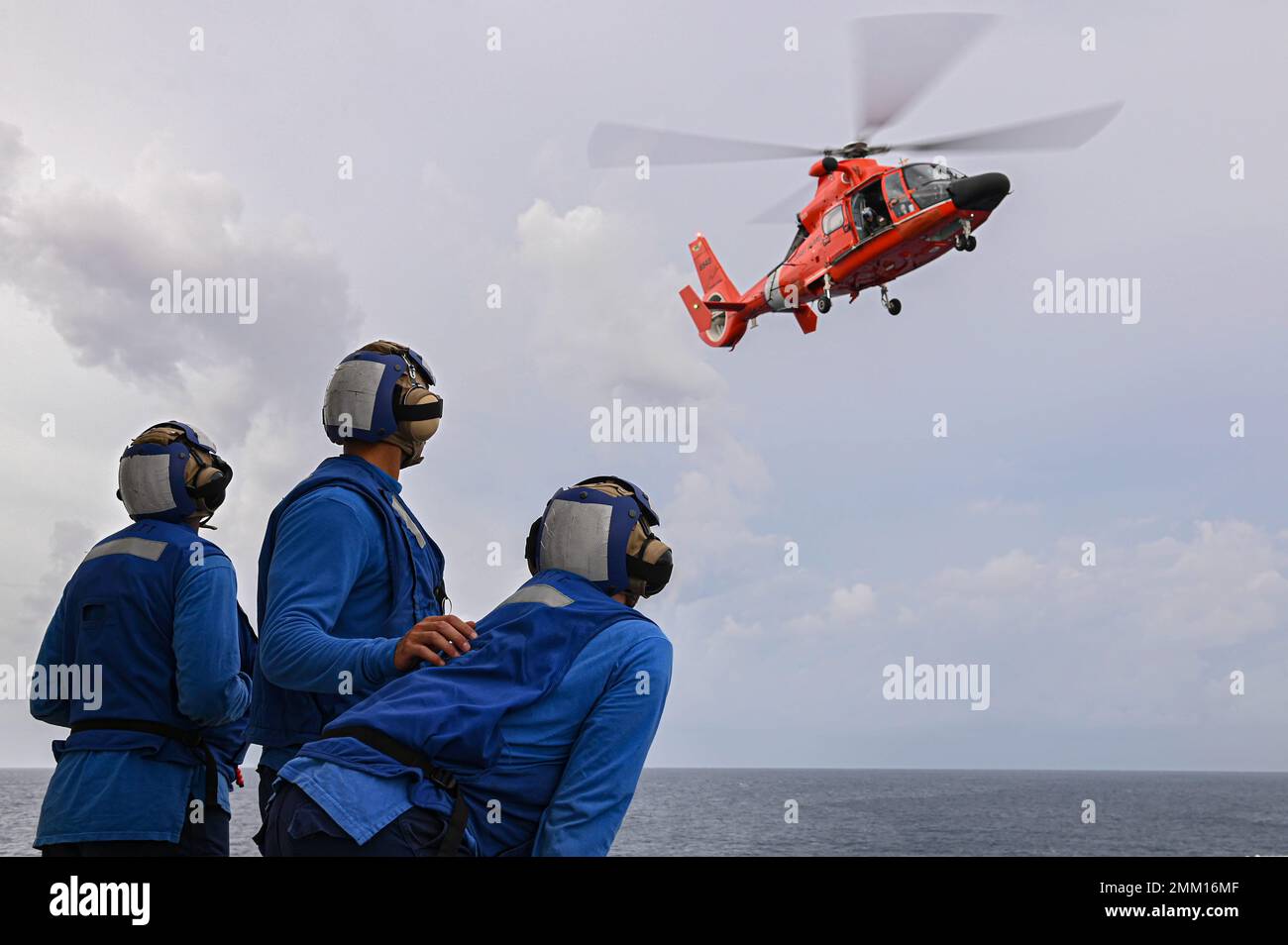 An MH-65 Dolphin helicopter from U.S. Coast Guard Air Station Barbers Point approaches for a landing while crewmembers aboard Coast Guard Cutter Midgett (WMSL 757) prepare to tie-down the aircraft after it lands on Sep. 13, 2022. The flight crew and helicopter are temporarily deployed in support of the 2022 Western Pacific patrol. Stock Photo