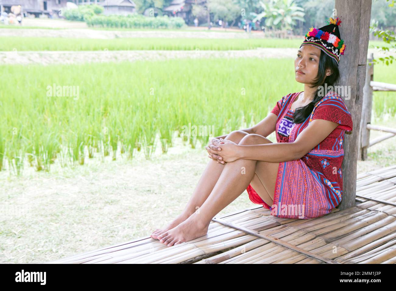Asian woman in traditional costume for Karen resting beside green rice field Stock Photo