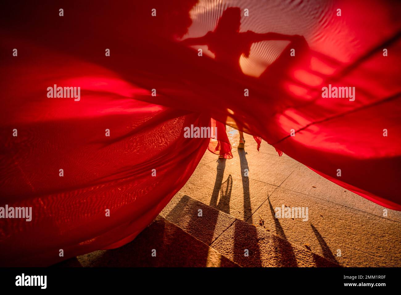 Sunrise red dress. A woman in a long red dress against the backdrop of sunrise, bright golden light of the sun's rays. The concept of femininity Stock Photo
