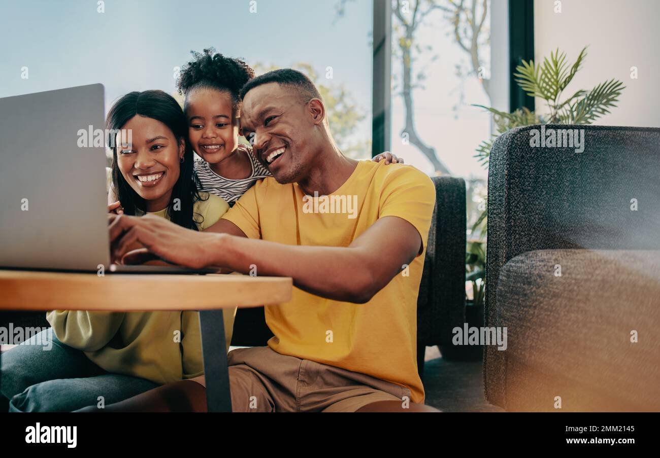 Searching for the perfect family movie, happy family of three browses a laptop for kid friendly programmes. Mom and dad spending time with their daugh Stock Photo