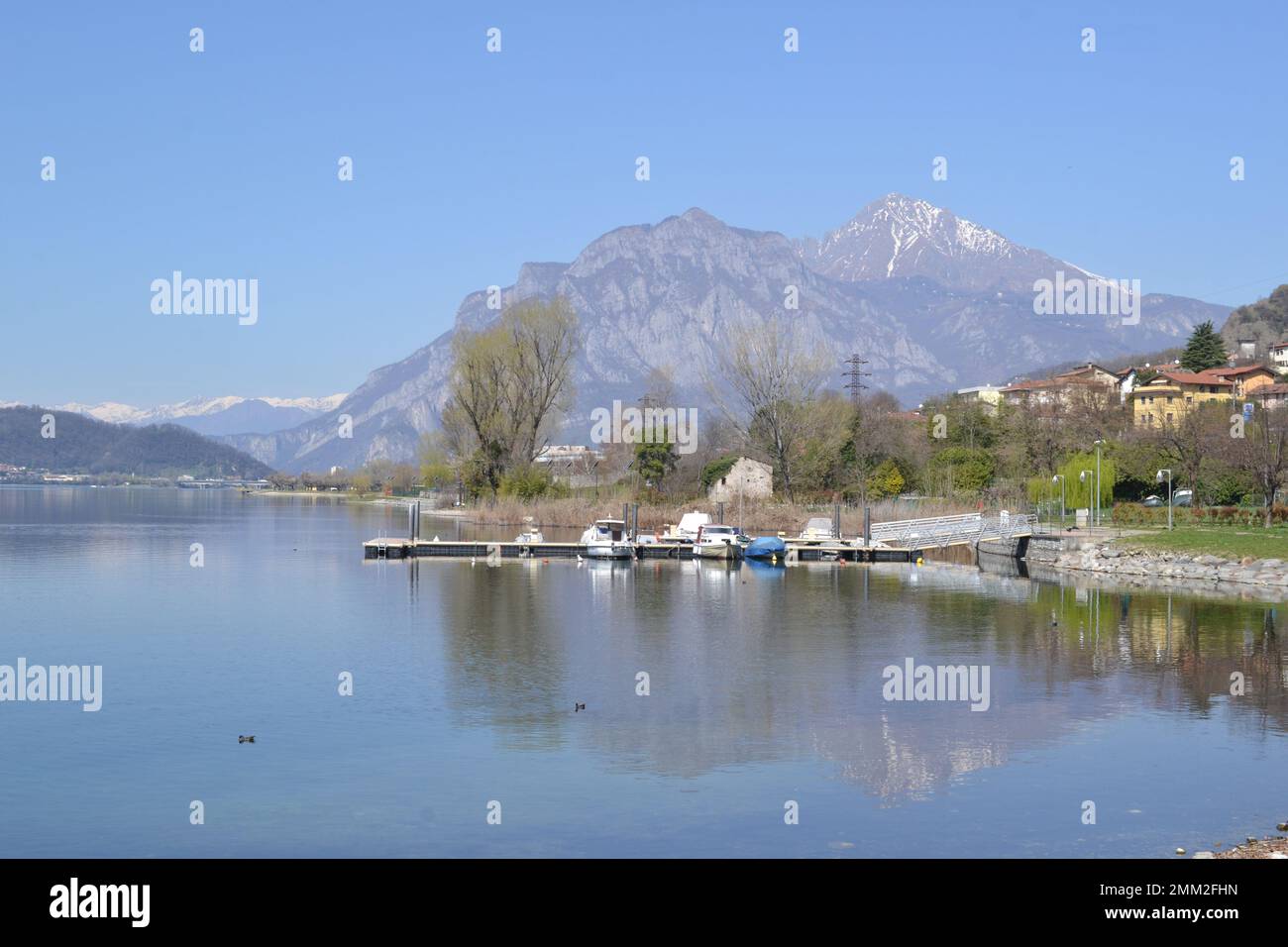 Beautiful panoramic landscape view of Lake Garlate at Lecco flowing from Lake Como in Italy. Small pier for motor boats in the foreground. Stock Photo