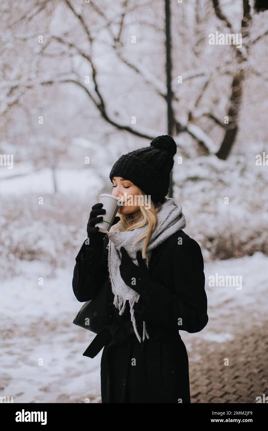 Pretty young woman n warm clothes enjoying in snow with takeaway coffee cup Stock Photo