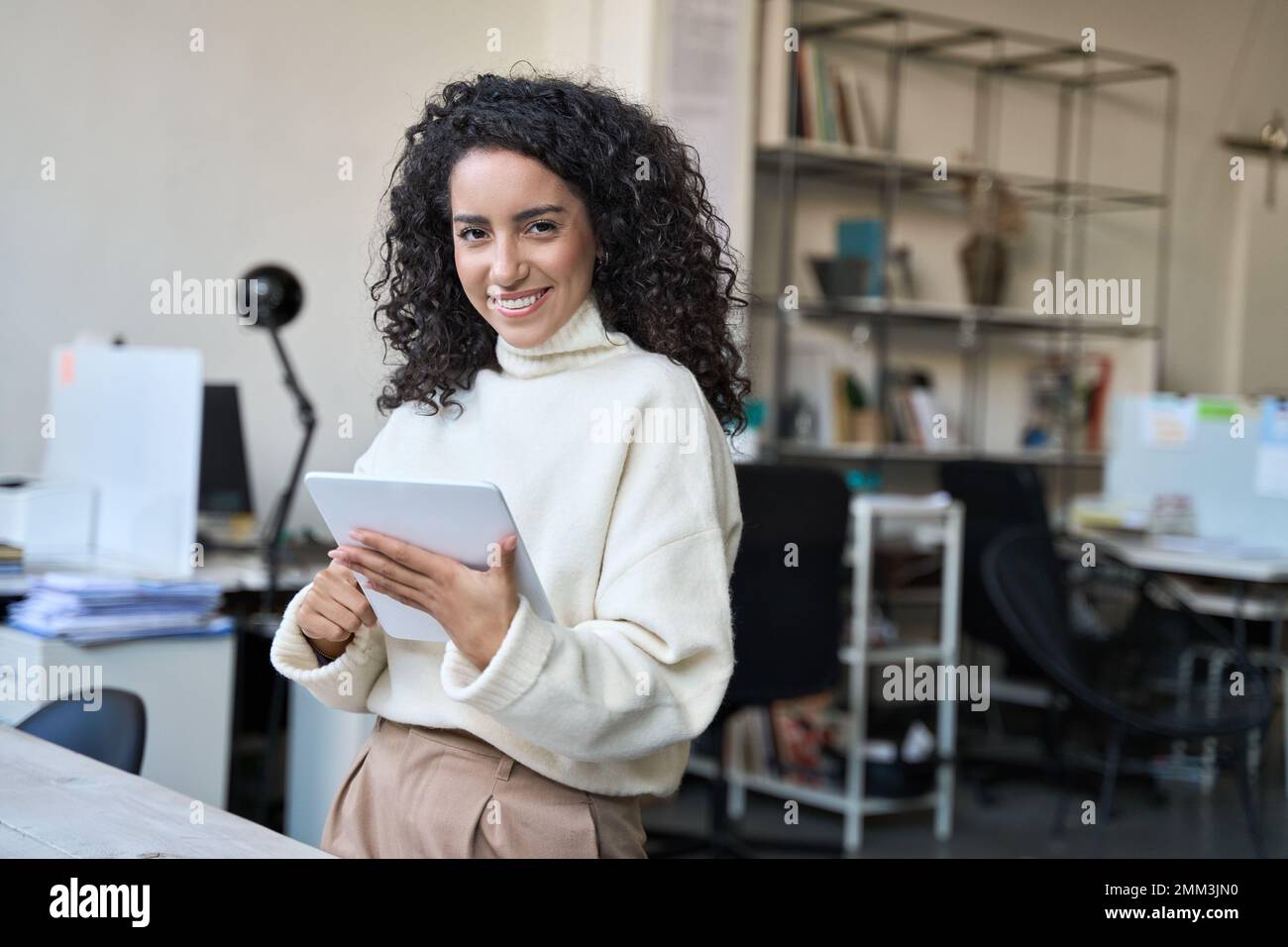 Smiling latin young professional business woman using digital tablet in office. Stock Photo